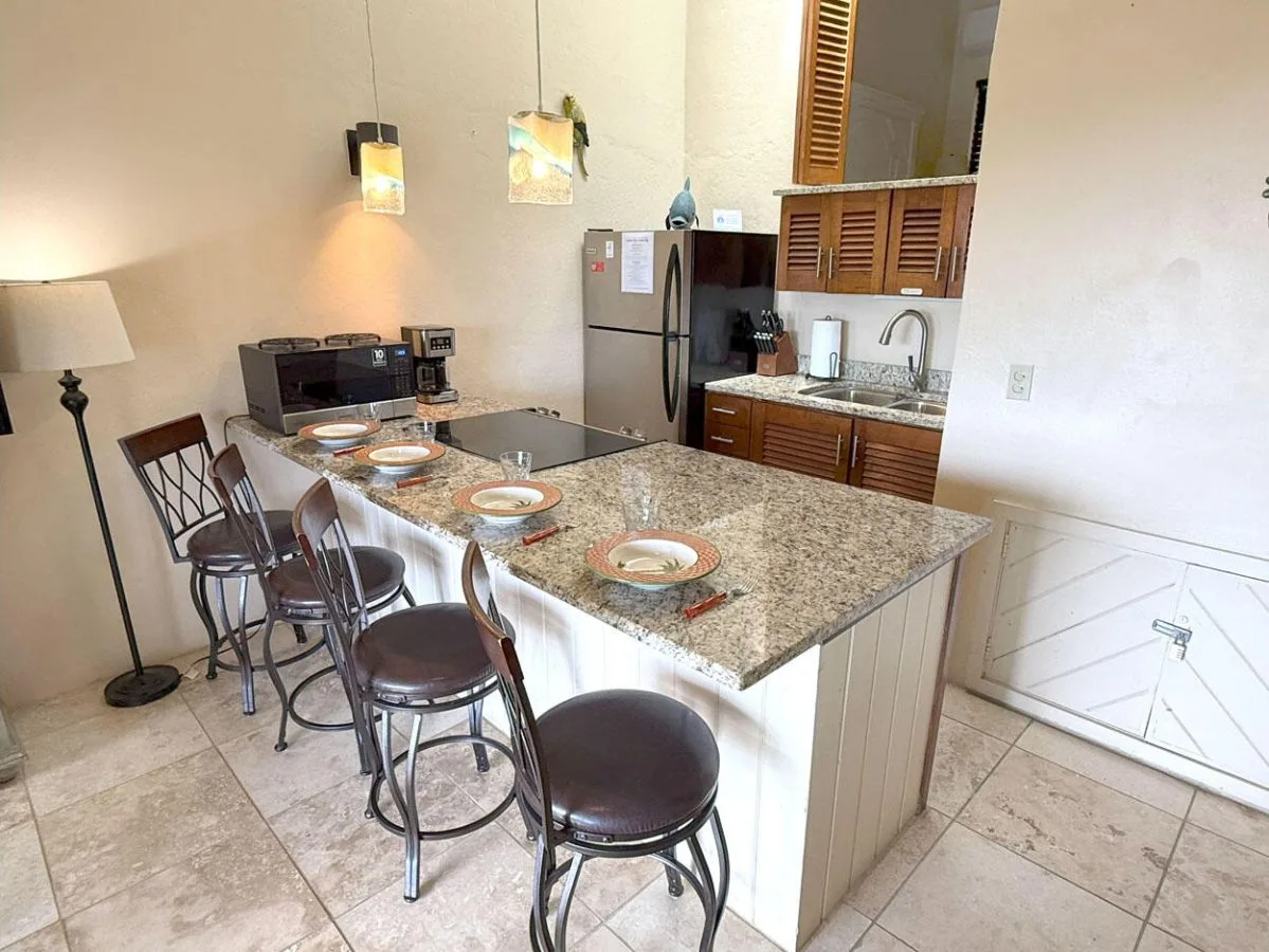 Una isla de cocina con asientos de barra y cubiertos está junto a la zona de cocina.