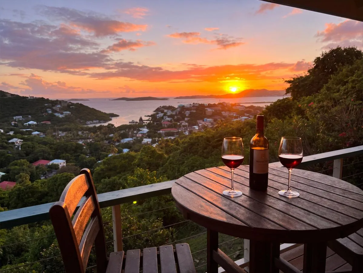 Atardecer sobre una bahía costera, visto desde una terraza con una mesa y copas de vino.