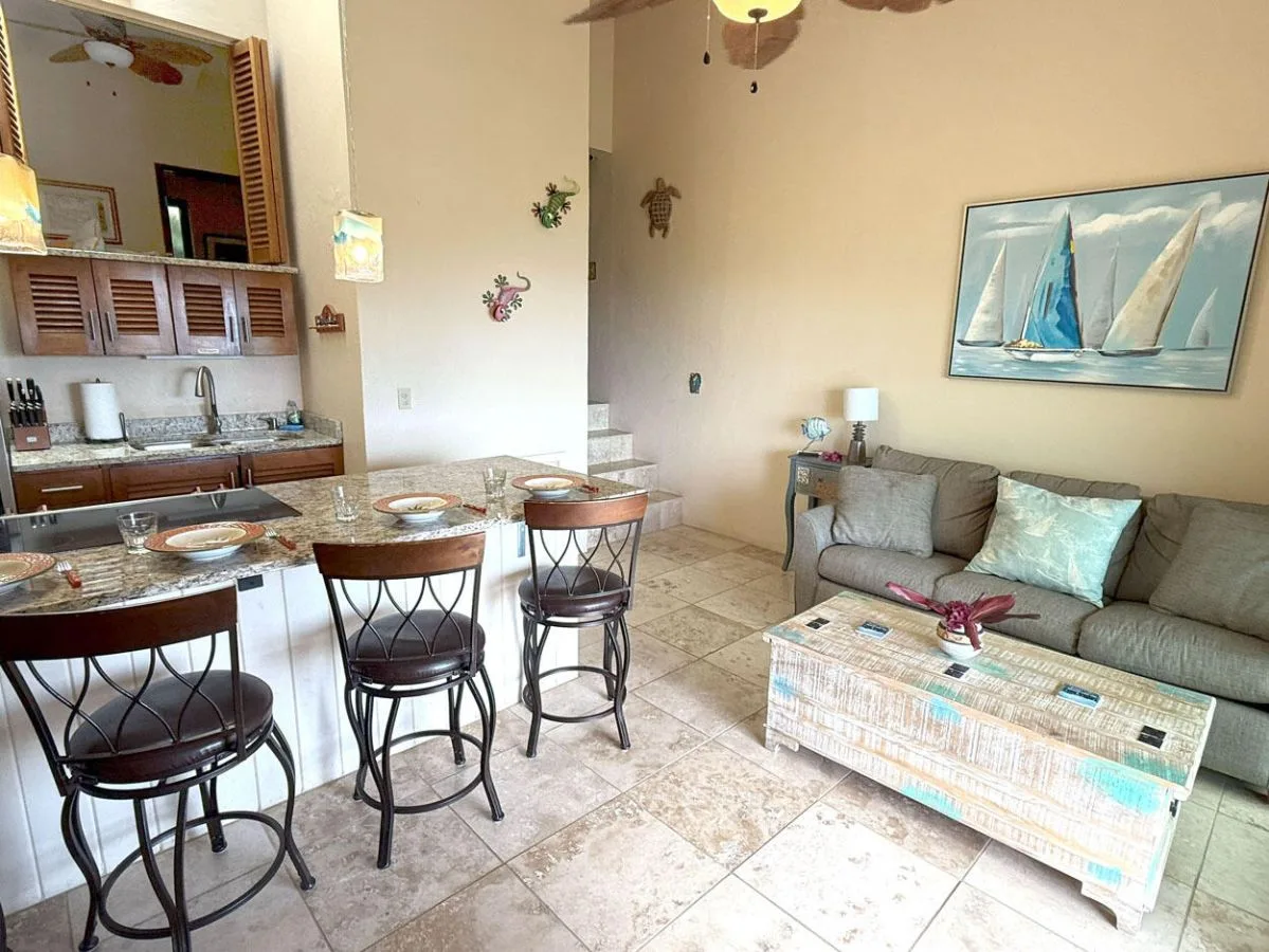 Una sala y comedor abiertos tienen un sofá junto a una mesa y una encimera de cocina.