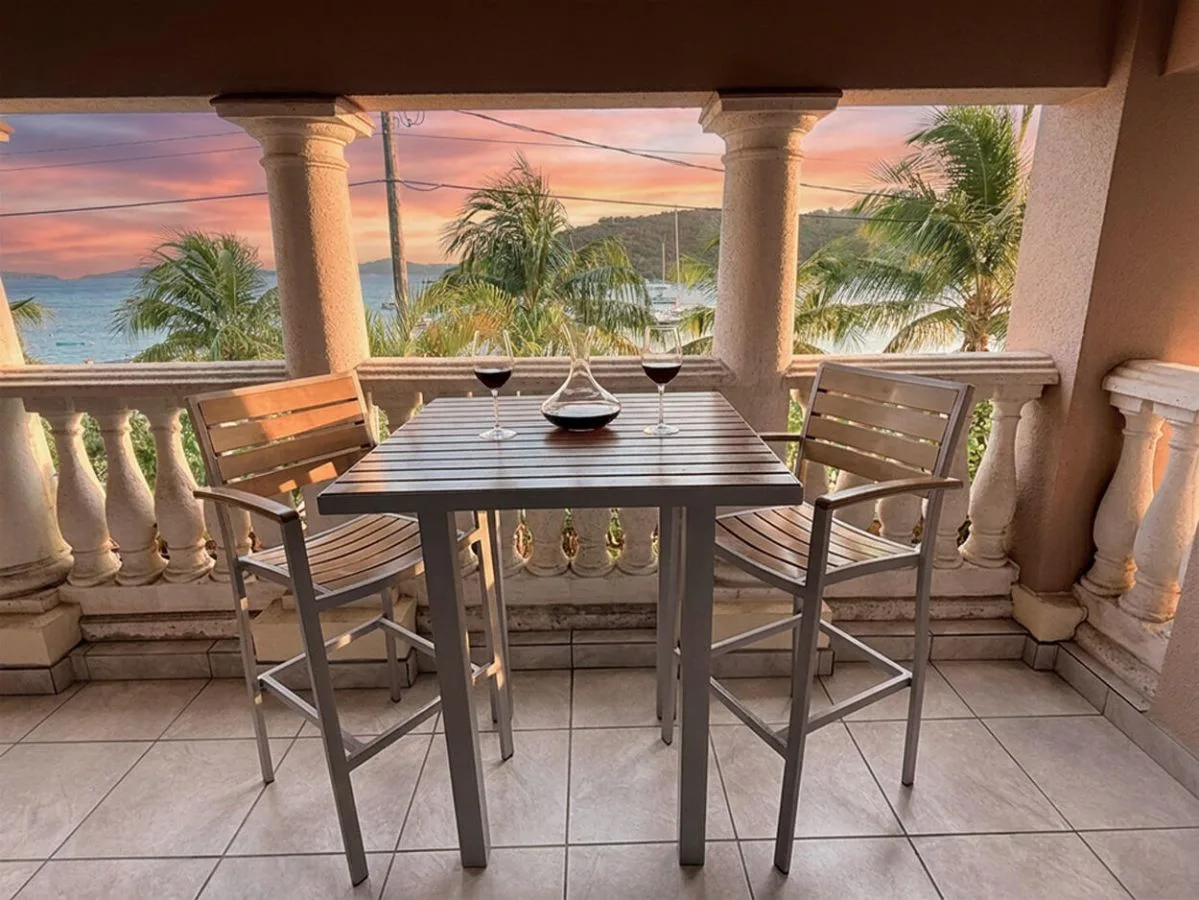 Un comedor en el balcón da a palmeras y al agua al atardecer.