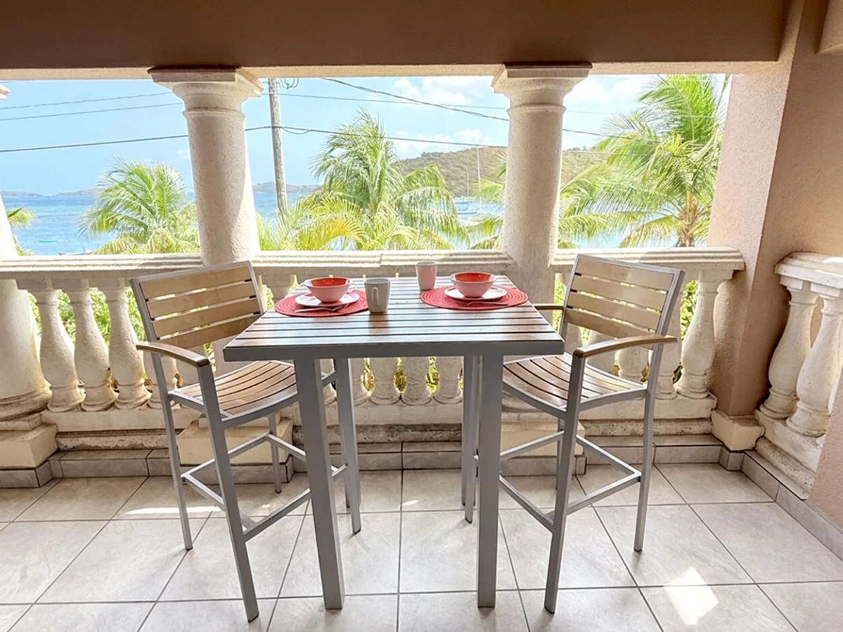 Una zona de comedor en un balcón cubierto, con mesa y asientos frente al agua.