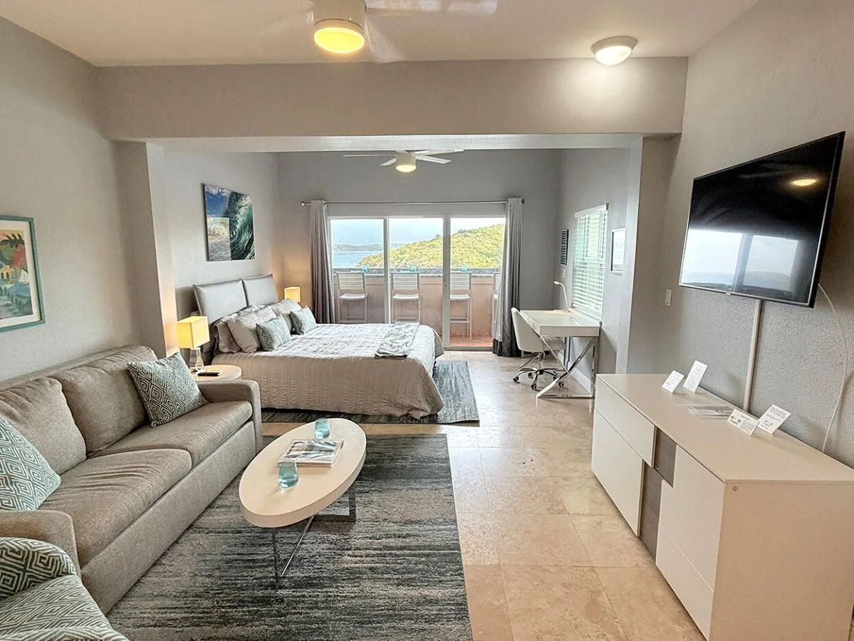 Dormitorio y zona de estar con cama, asientos y un televisor montado en la pared.