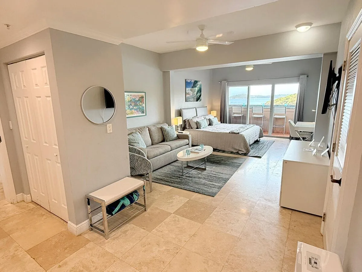 Un estudio luminoso con una cama, una zona de estar y puertas al balcón.