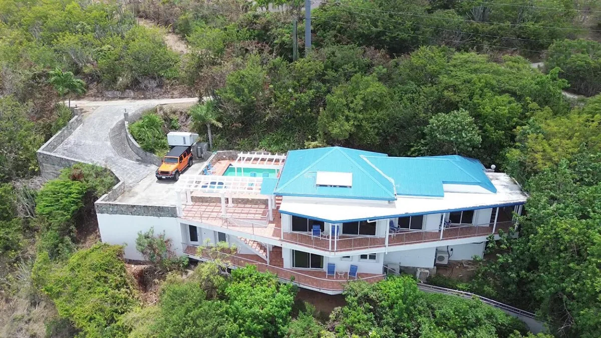 Una vista aérea muestra una casa con techos azules rodeada de abundante vegetación.