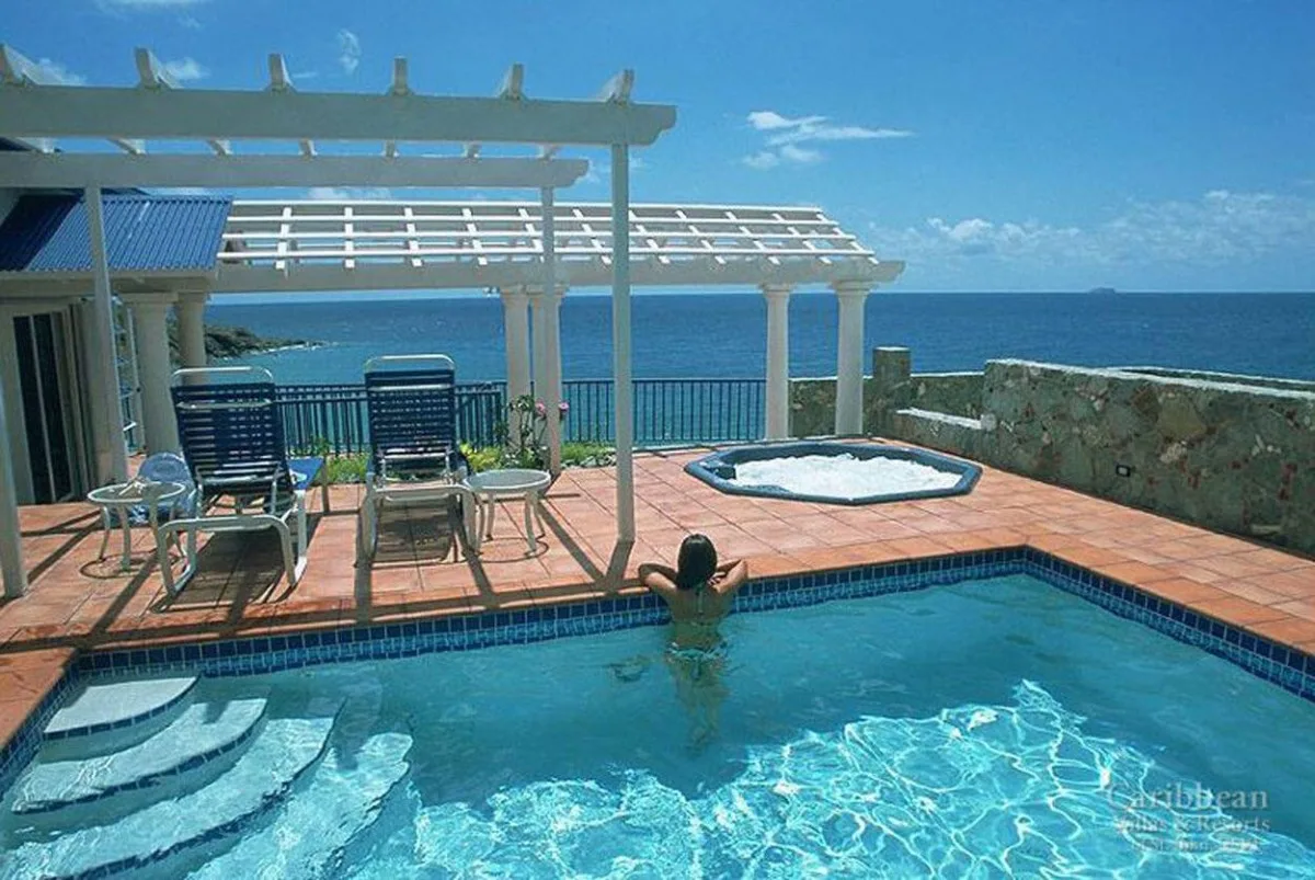 Una piscina y un jacuzzi elevado miran al océano junto a un patio sombreado.