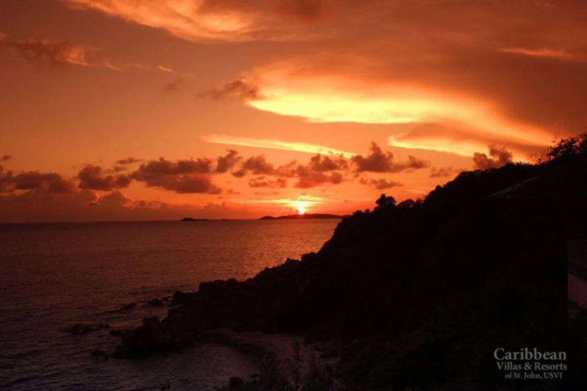 Un atardecer intenso ilumina el mar junto a una costa rocosa oscura.