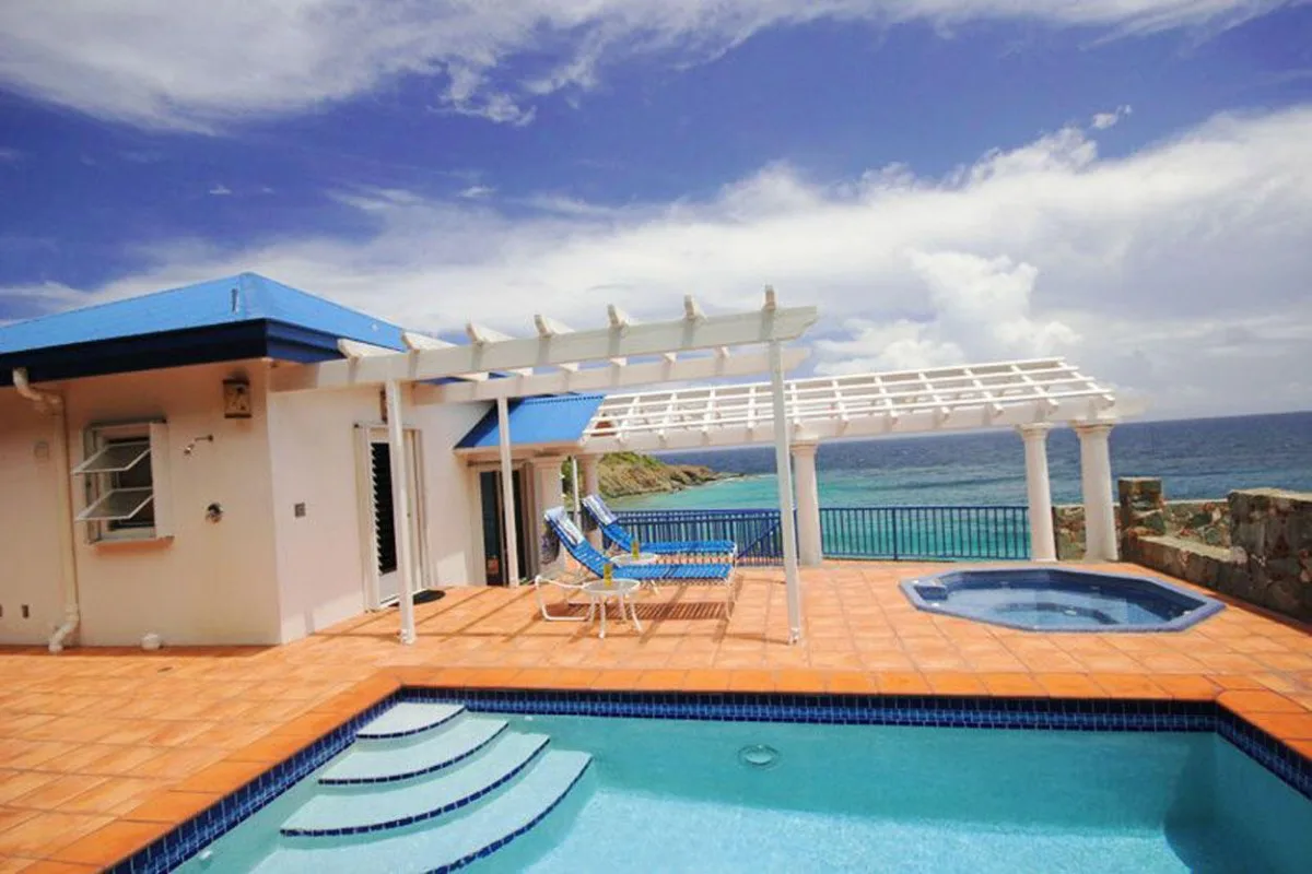 Una piscina exterior y una terraza dan al mar junto a un edificio blanco.