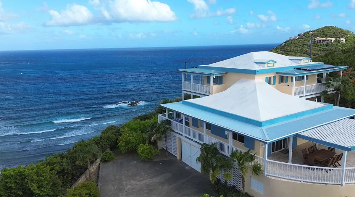 A coastal house with blue roofs overlooks the ocean.