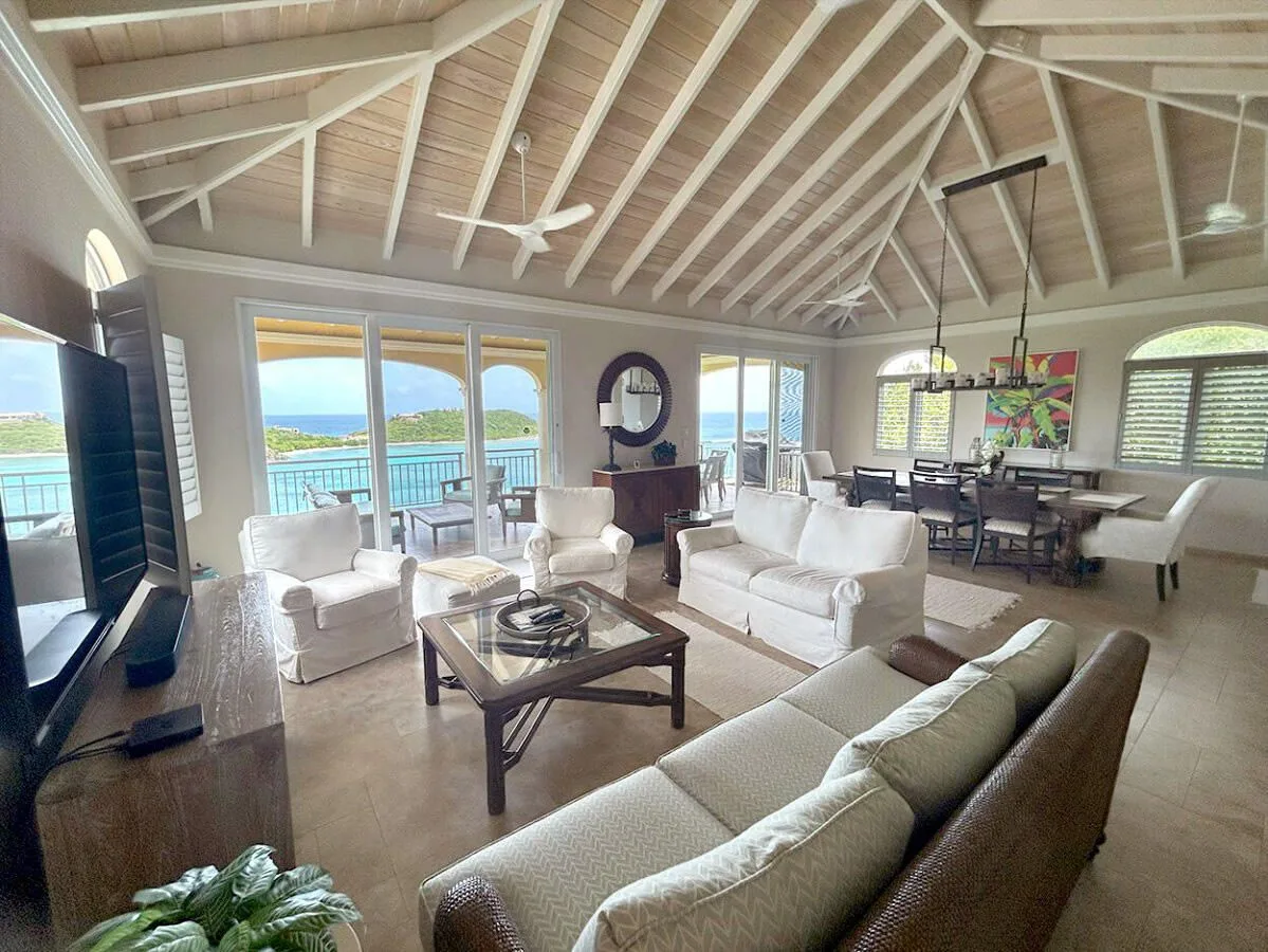 Una sala de estar con asientos, una mesa de centro y grandes ventanas con vista al agua.