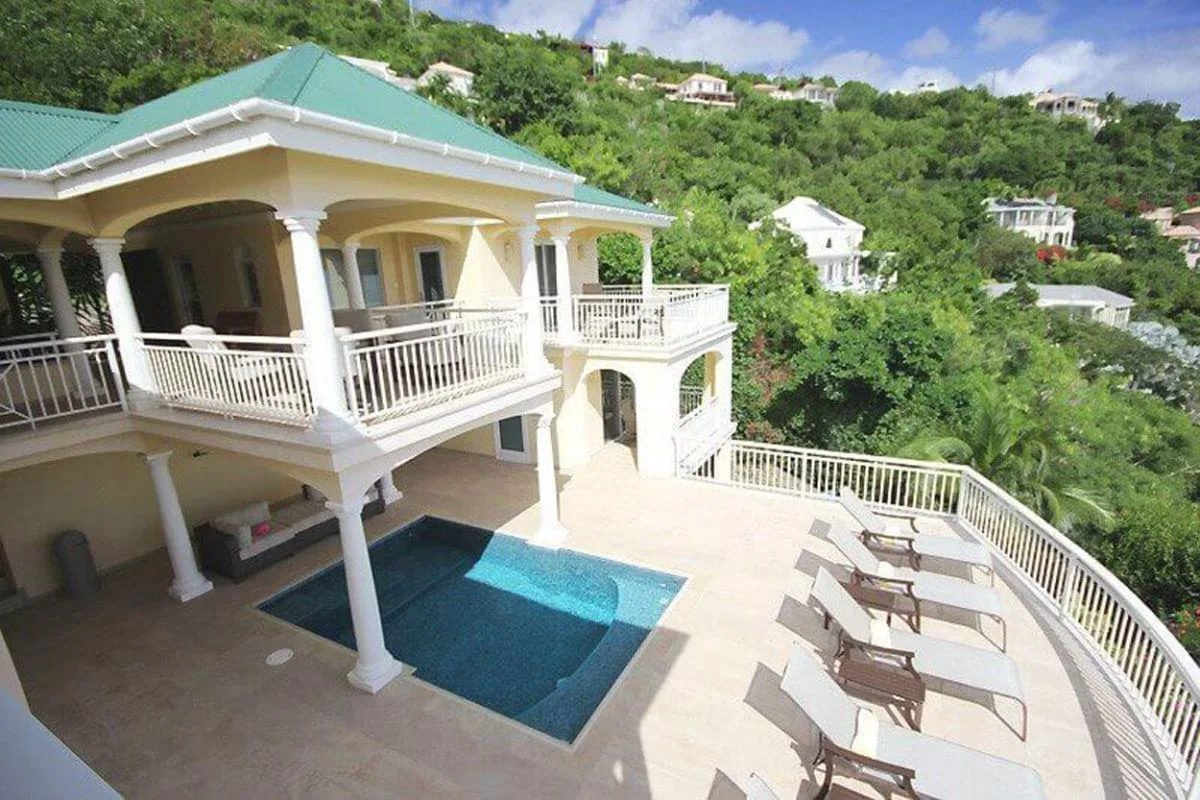 Una casa en una ladera tiene balcones cubiertos con vista a una piscina y una zona de estar al aire libre.