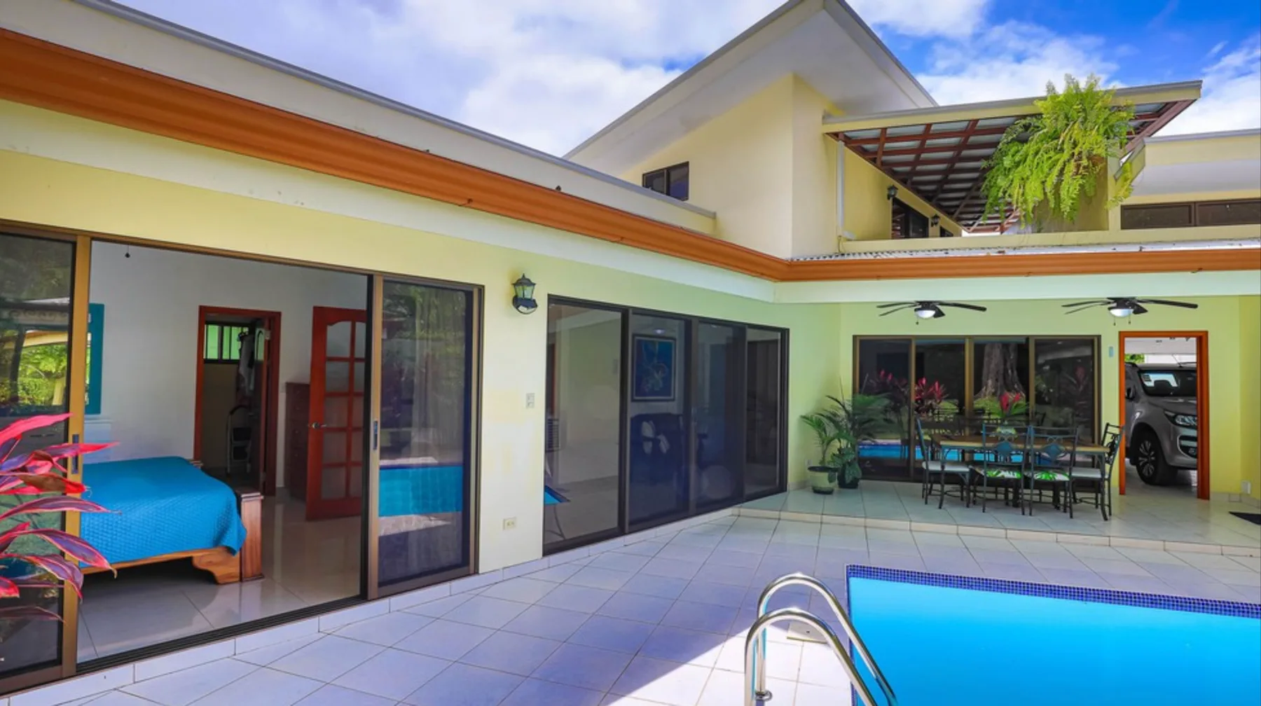 A tiled courtyard patio surrounds a swimming pool beside a modern house.