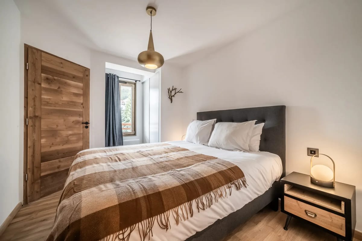 Dormitorio moderno con una cama grande, ropa de cama blanca, cabecero gris y lámparas de mesilla.