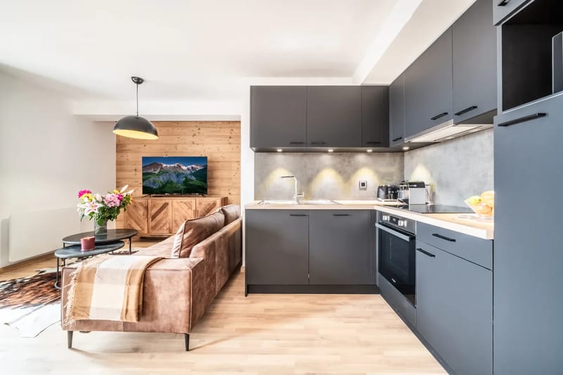Cocina totalmente equipada y salón de planta abierta, con armarios de color gris oscuro y detalles de madera.