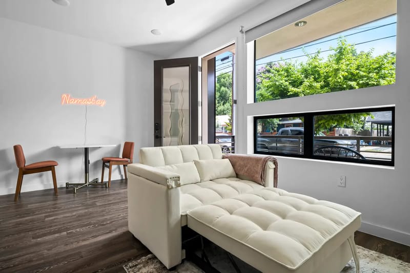Habitación moderna con una chaise longue blanca, una mesa pequeña y dos sillas.