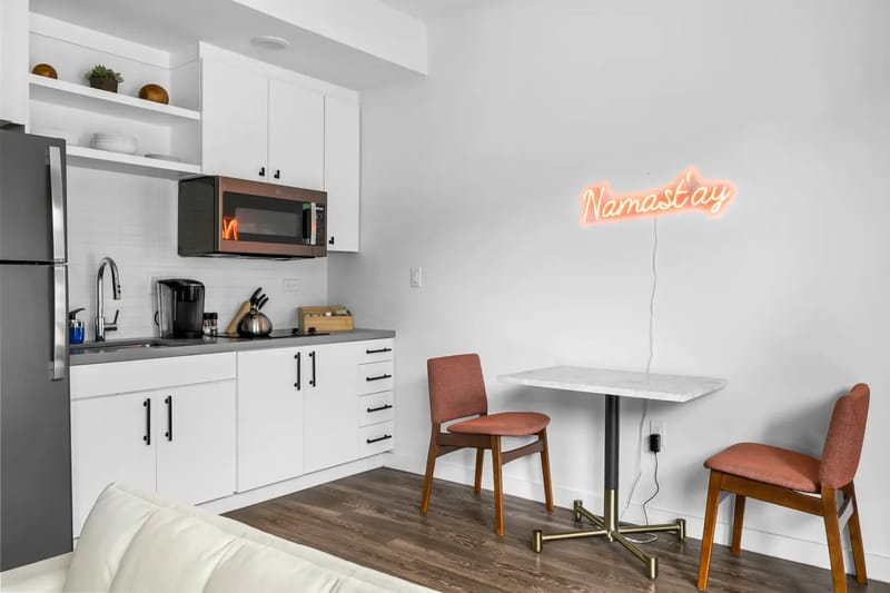 Pequeña cocina moderna con gabinetes blancos, electrodomésticos de acero inoxidable y un pequeño comedor.