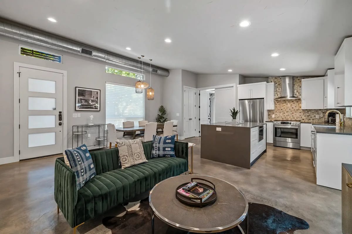 Modern open-plan living space with a green sofa, dining area, and kitchen.