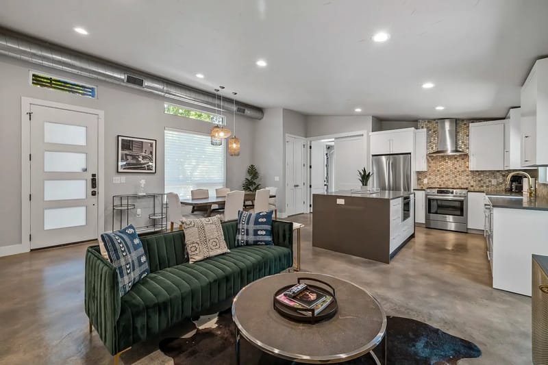 Modern open-plan living space with a green sofa, dining area, and kitchen.