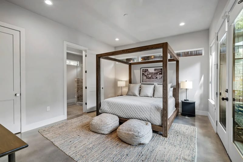 Contemporary bedroom with a wooden canopy bed, large windows, and a view of greenery.