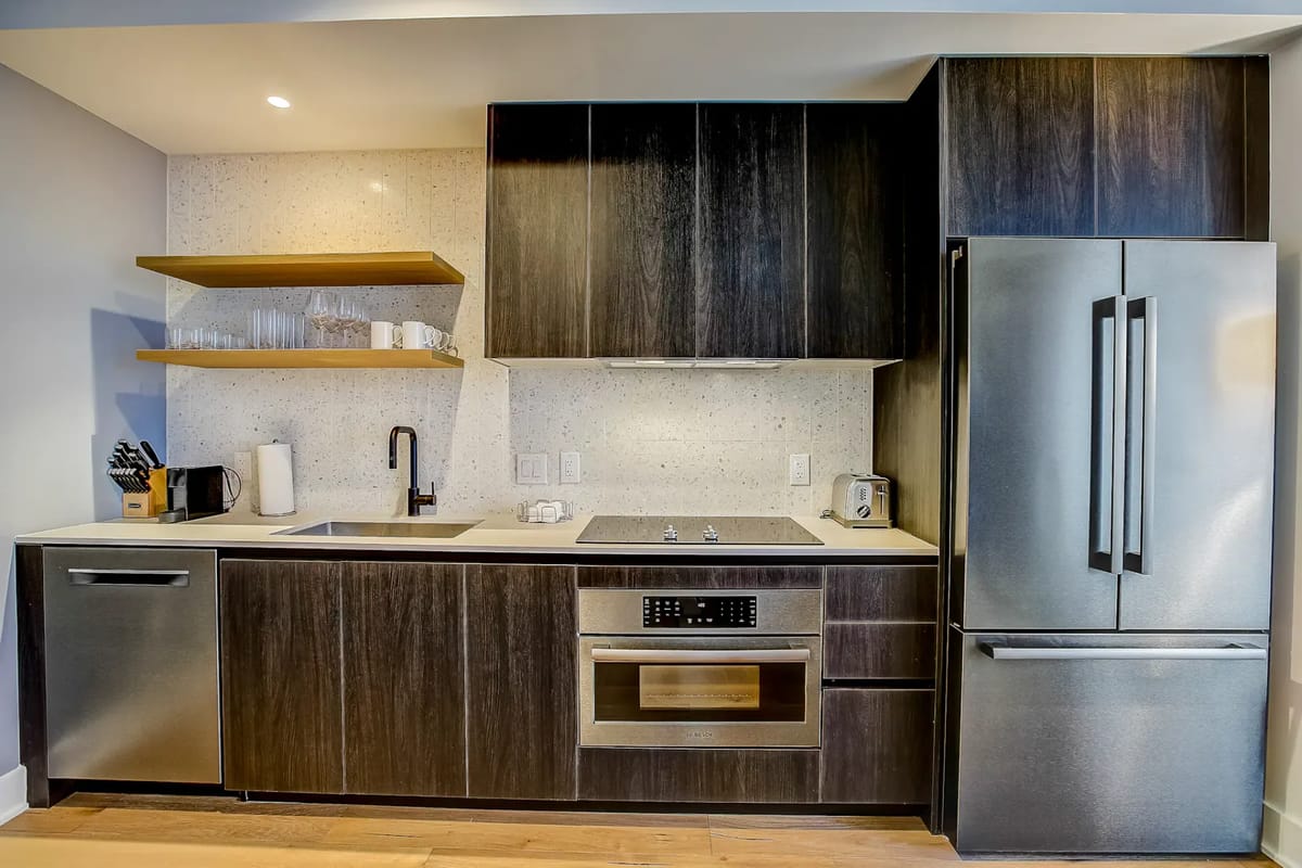 Cocina moderna con gabinetes oscuros, electrodomésticos de acero inoxidable y encimera de color claro.