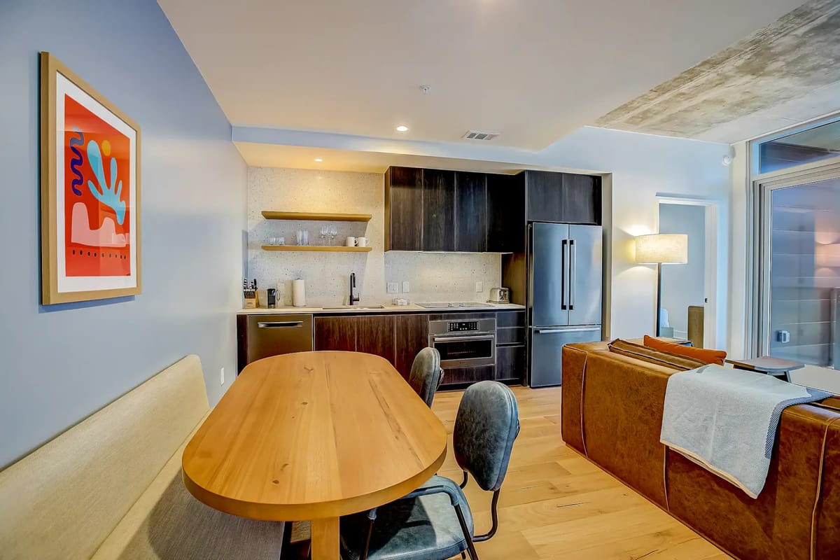 Cocina y comedor de concepto abierto con mesa de madera, gabinetes oscuros, sofá y obras de arte.