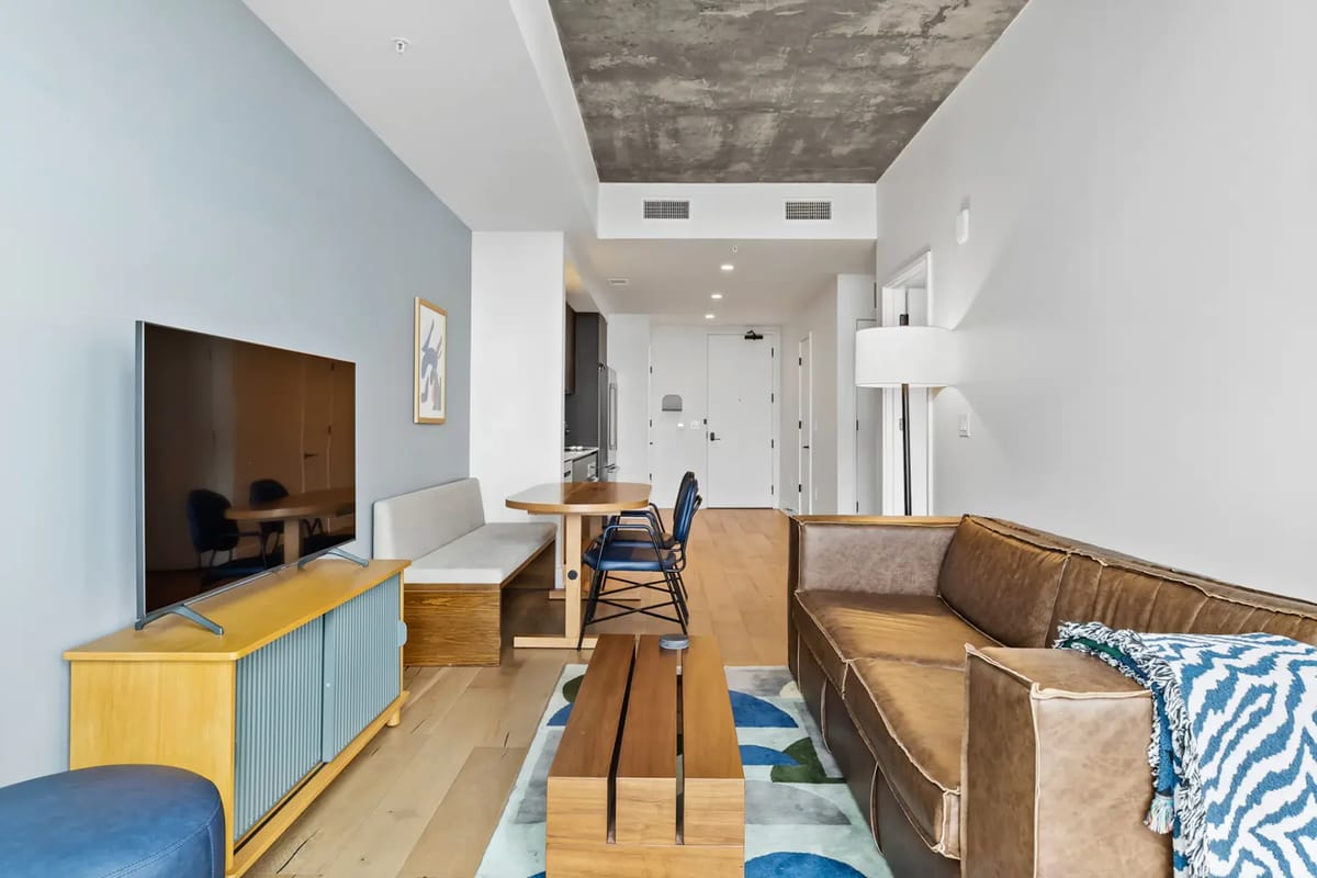 Modern living room with a brown sofa, wooden coffee table, wall-mounted TV, and dining area.