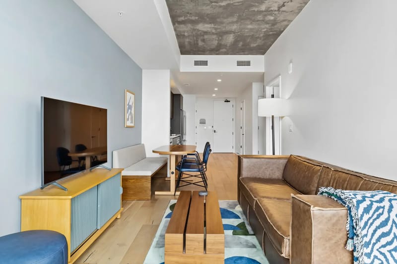 Sala de estar moderna con un sofá marrón, una mesa de centro de madera, un televisor montado en la pared y un comedor.