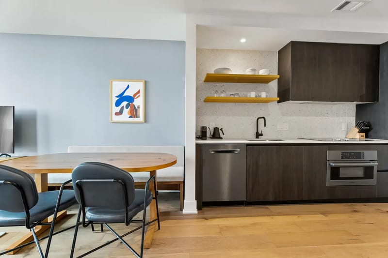 Cocina y comedor modernos con gabinetes oscuros, electrodomésticos de acero inoxidable y una encimera de color claro.