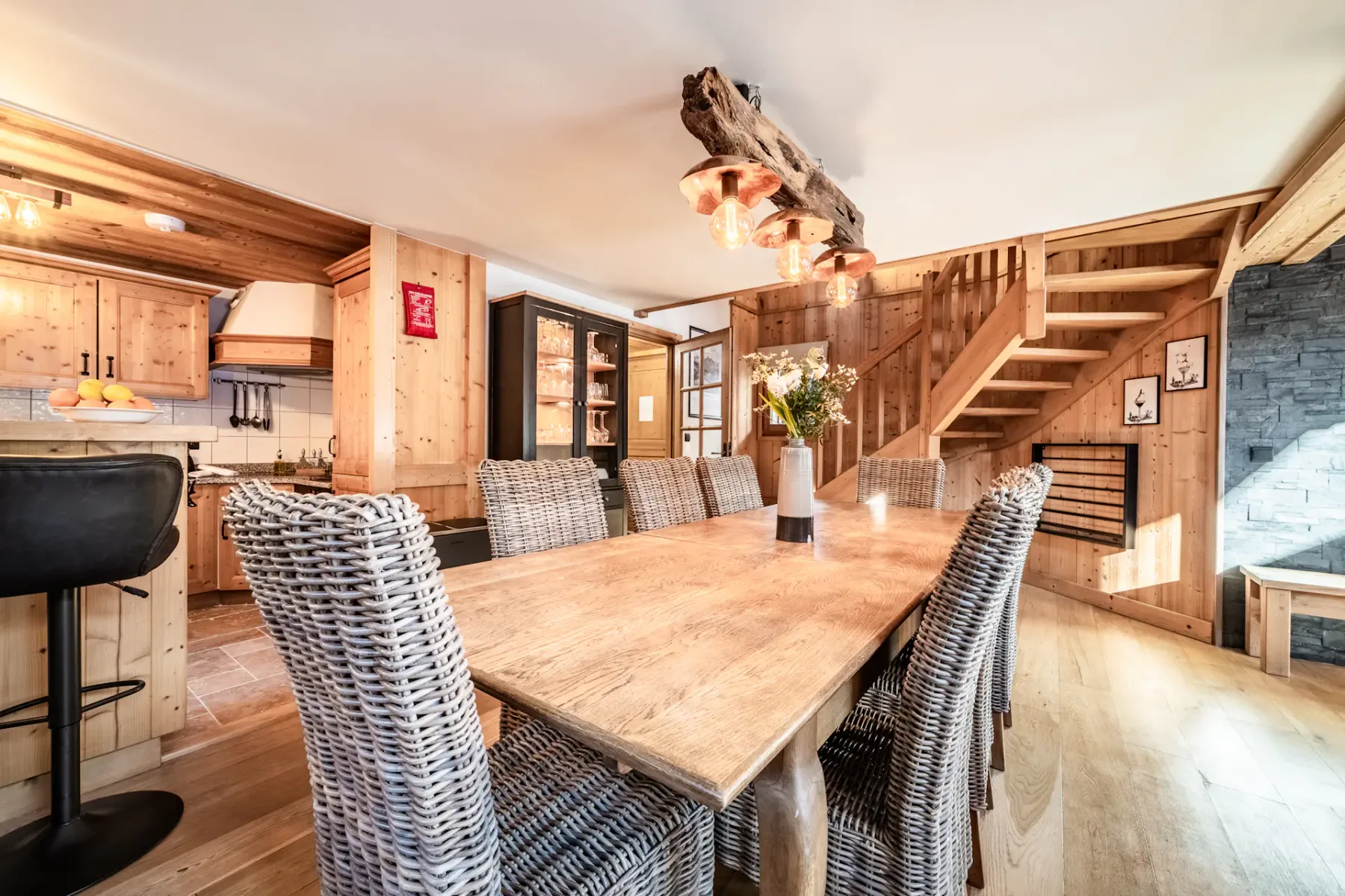 Rustic dining room with a wooden table, wicker chairs, and a bar area.