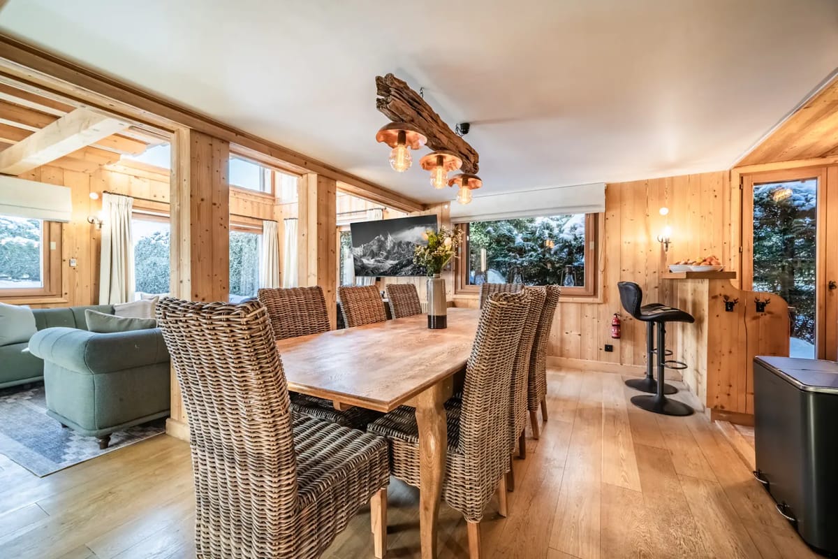 Comedor rústico con una mesa de madera, sillas de mimbre y vistas al paisaje nevado.