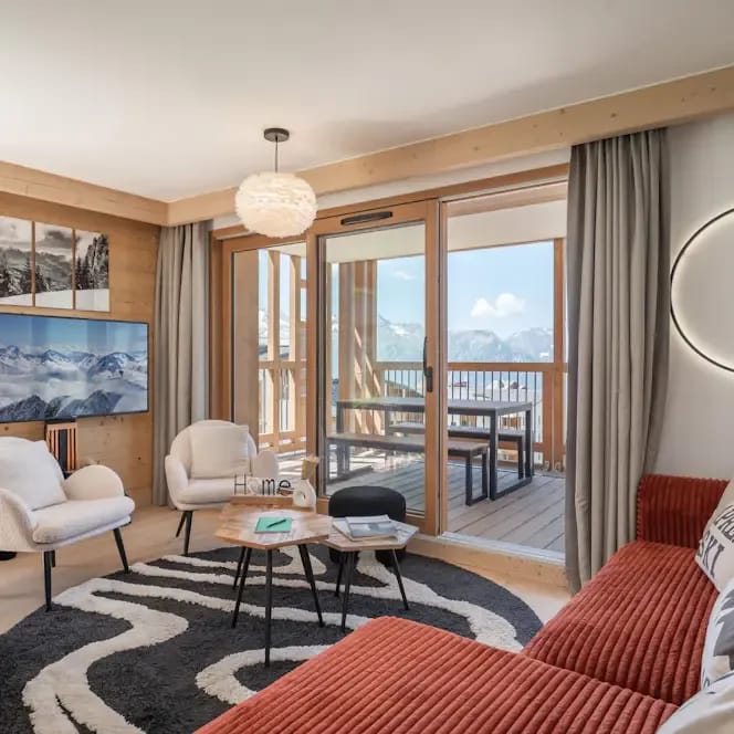 Bright modern living room with red sofa, white armchairs and balcony access with mountain views.