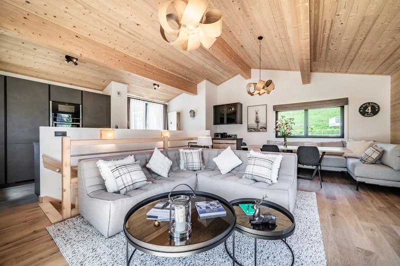 Cozy living room with wooden ceiling, plush sectional sofa, modern fireplace, round coffee table, and large window overlooking a scenic view.