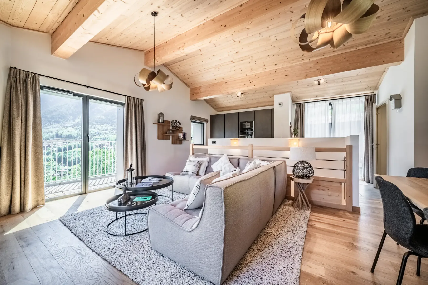 Acogedor salón con techo de madera, cómodo sofá modular, chimenea moderna, grandes ventanas y un jarrón con flores sobre la mesa.