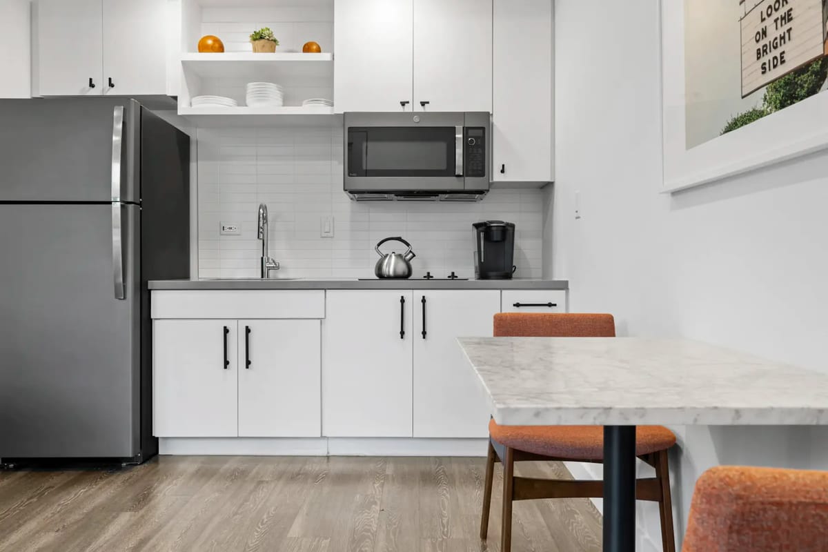 Cocina con refrigerador, microondas, hervidor de agua y mesa de comedor.