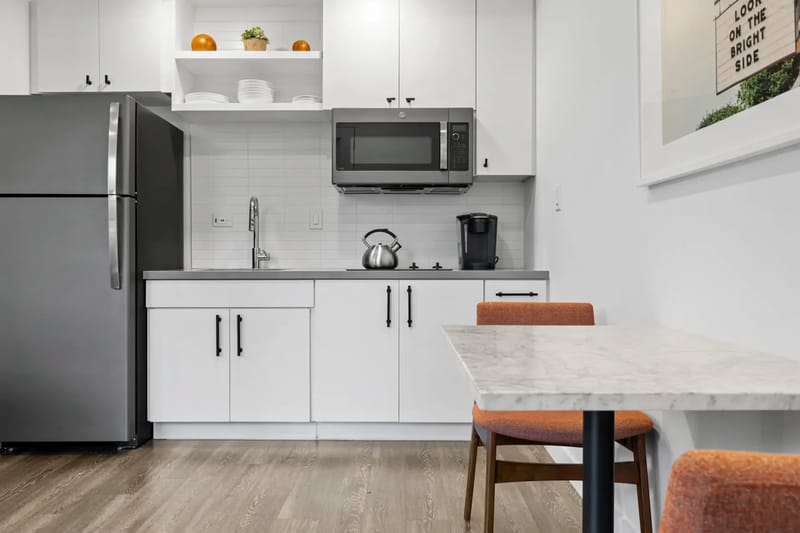 Cocina con refrigerador, microondas, hervidor de agua y mesa de comedor.