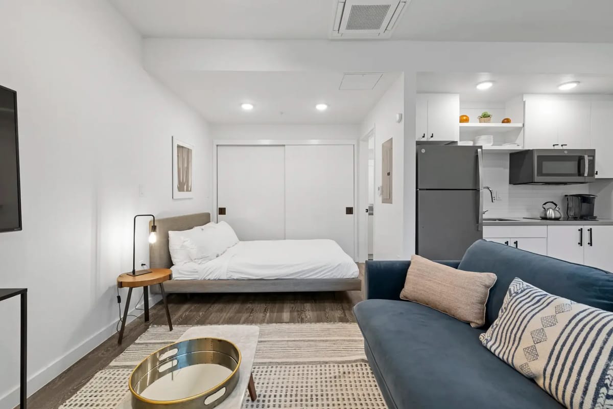 Apartamento tipo estudio moderno con un sofá azul, una cama y una cocina pequeña.