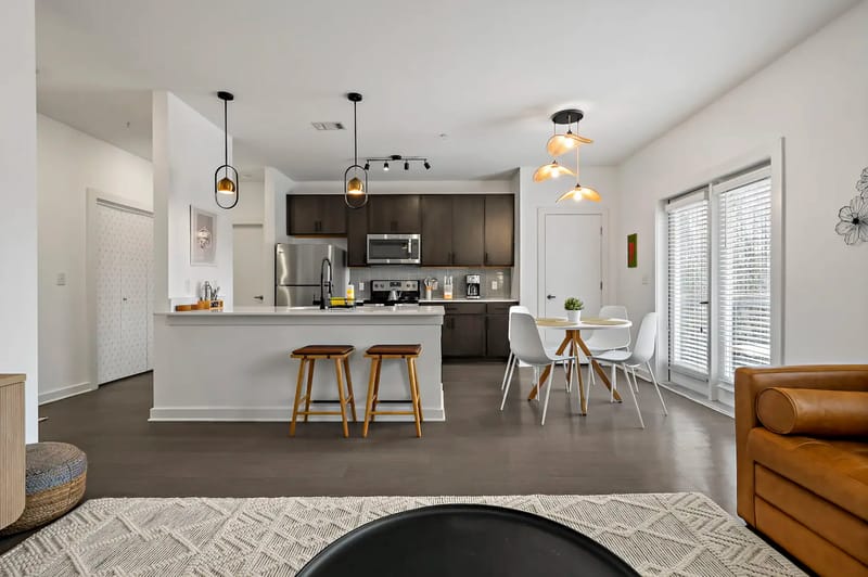 Cocina y comedor modernos de concepto abierto con gabinetes oscuros, iluminación colgante, una mesa de comedor redonda y taburetes en la isla, con luz natural.
