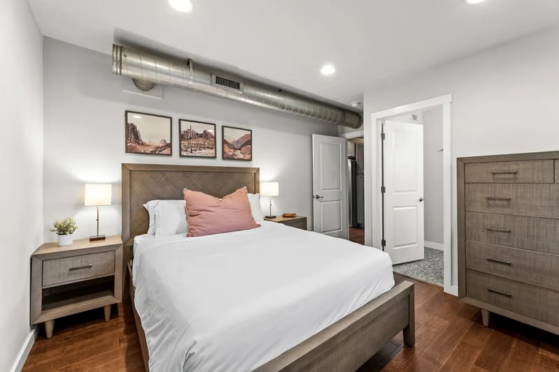 Modern bedroom with a double bed, white linens, wooden furniture, and artwork.