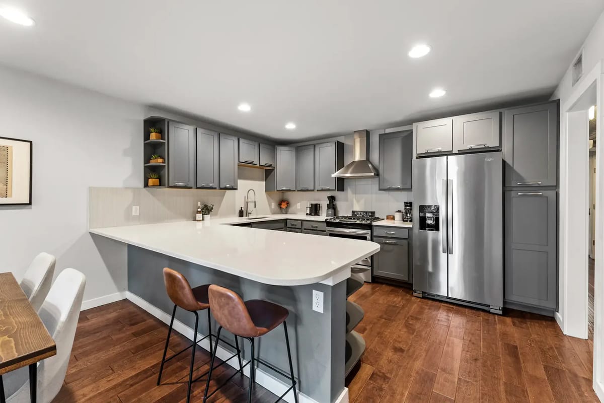 Modern kitchen with gray cabinets, stainless steel appliances, and a white countertop island.