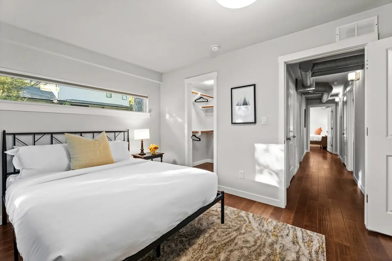 Modern bedroom with a white bed, rug, and bedside table.