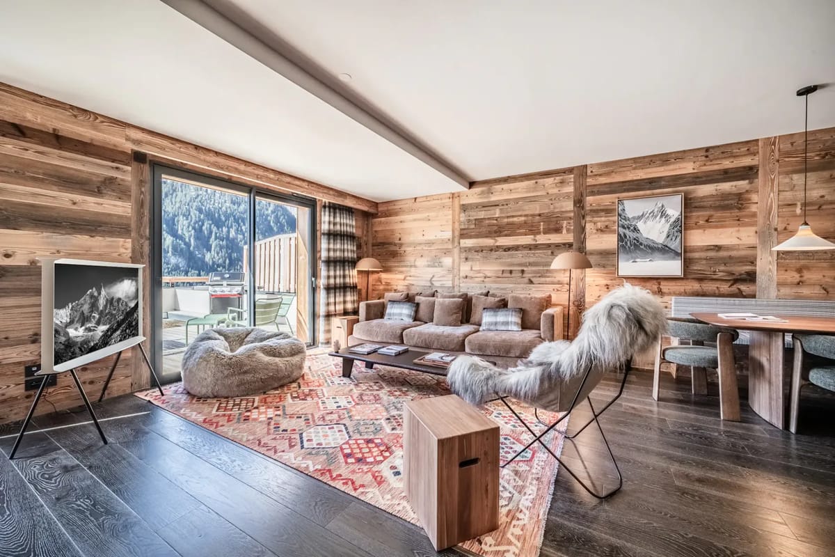 Cozy living room with wooden walls, plush seating, and a large window revealing a scenic mountain view.