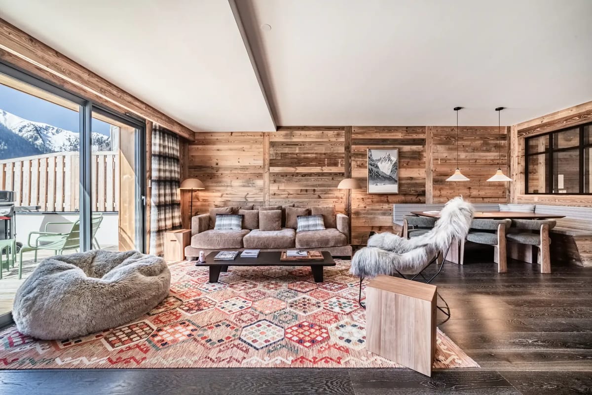 Cozy living room with wooden walls, plush seating, and a large window revealing a scenic mountain view.