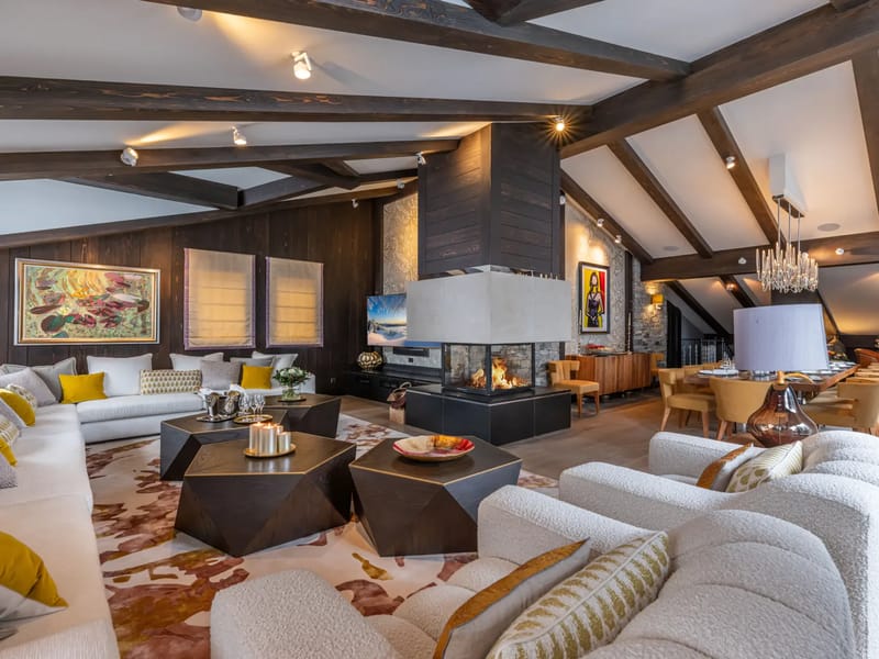 Spacious living room with modern decor, white sofas, a central fireplace, and exposed wooden beams.