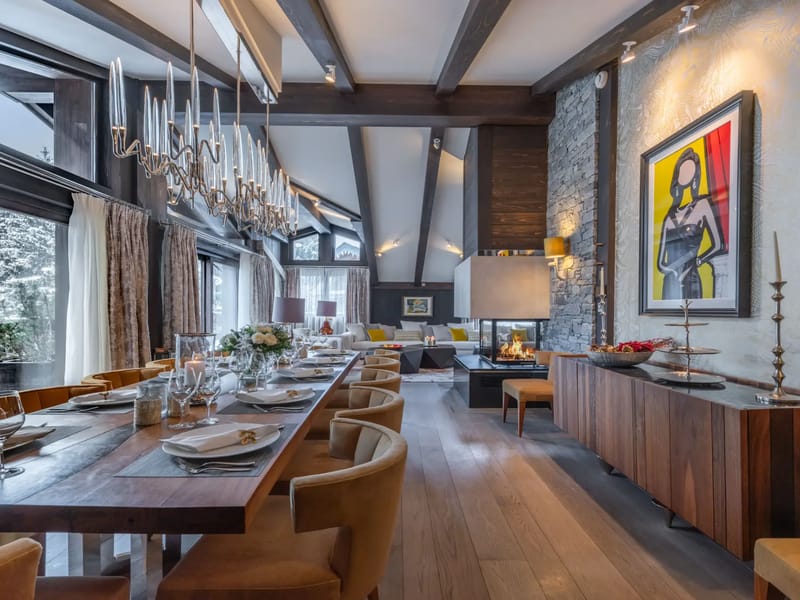 Elegant dining room with a long wooden table, modern chandelier, stone fireplace, and artwork.