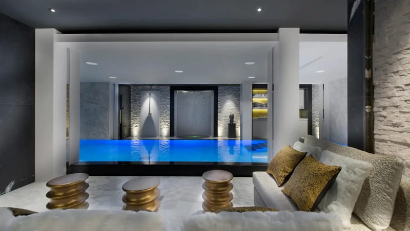 Indoor pool area with blue lighting, modern decor, sofas, and accent tables.