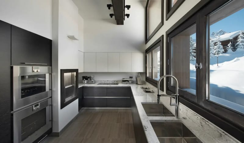 Modern kitchen with black and white cabinetry, stainless steel appliances, and mountain views.