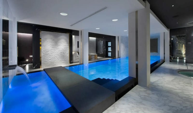 Indoor pool area with modern design, blue lighting, stone walls, and a small waterfall.