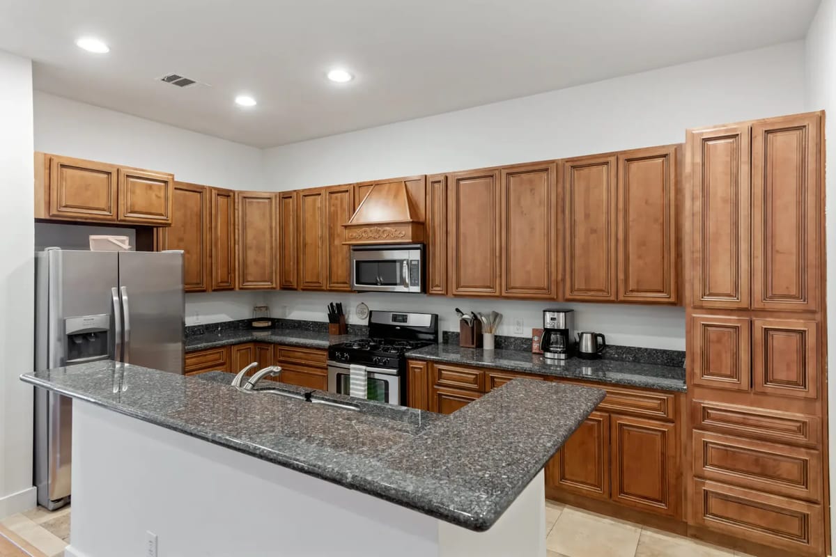 Modern kitchen with wooden cabinets, granite countertops, stainless steel appliances, and tile flooring. Bright, well-lit space.
