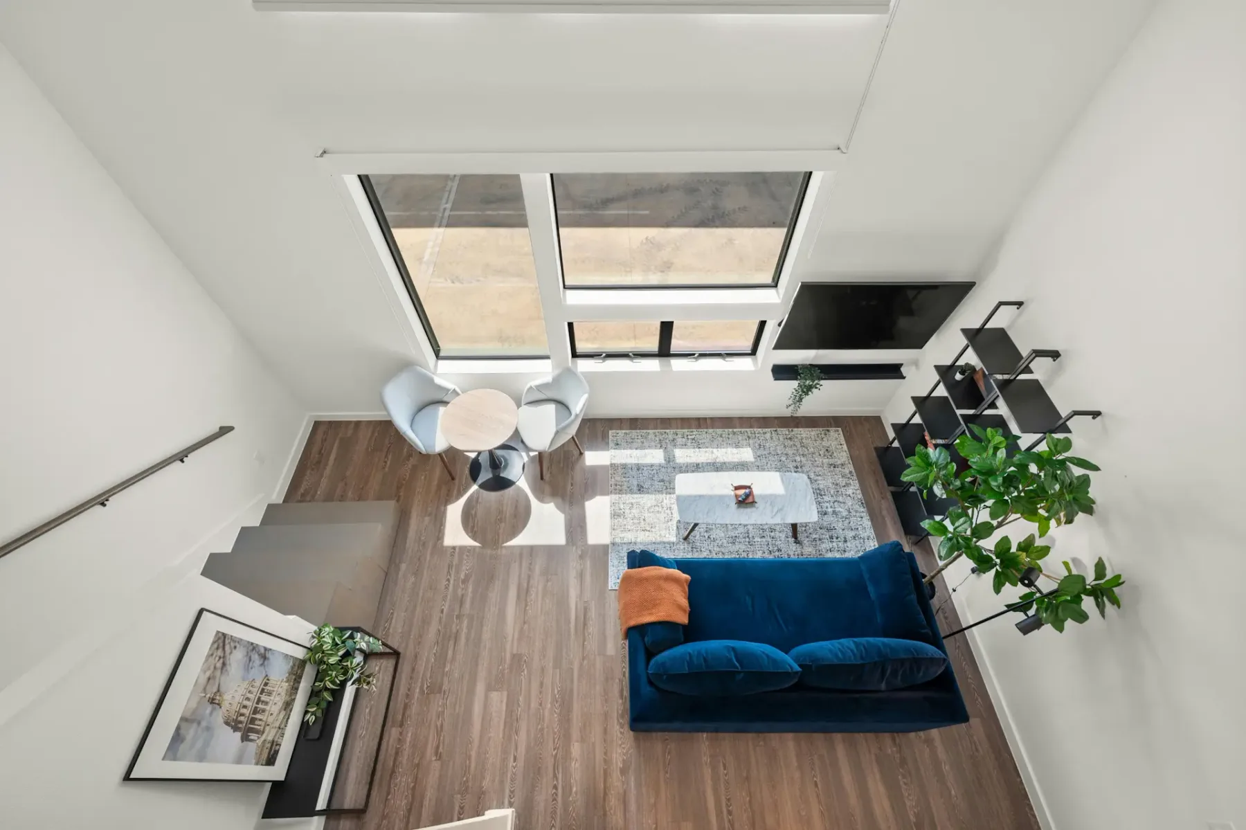Modern open-plan living area with blue sofa, kitchenette, round table, and large windows.