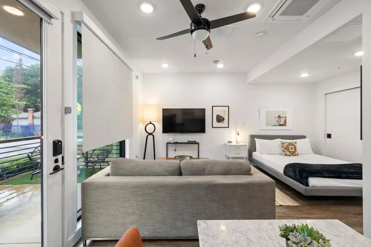 Apartamento tipo estudio moderno con sofá, TV, cama y ventilador de techo.