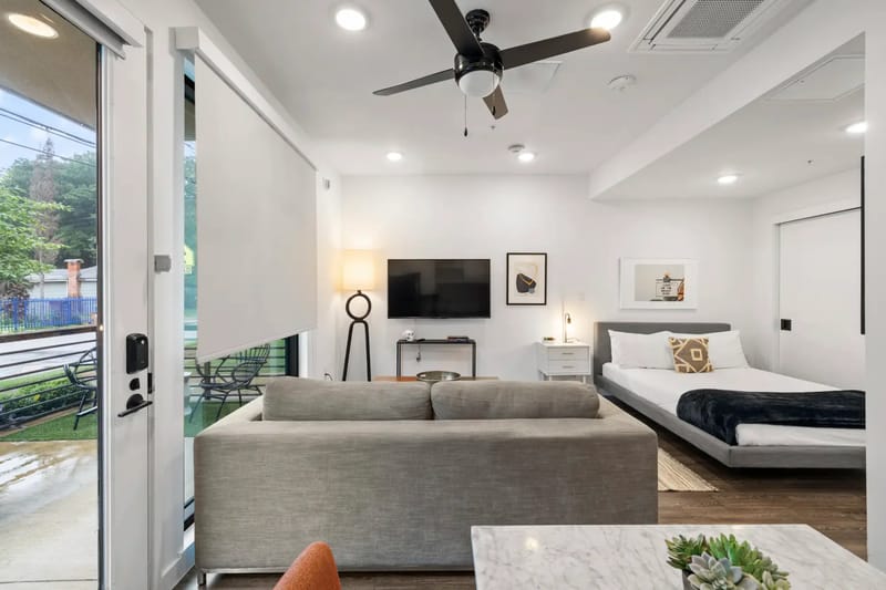 Apartamento tipo estudio moderno con sofá, TV, cama y ventilador de techo.